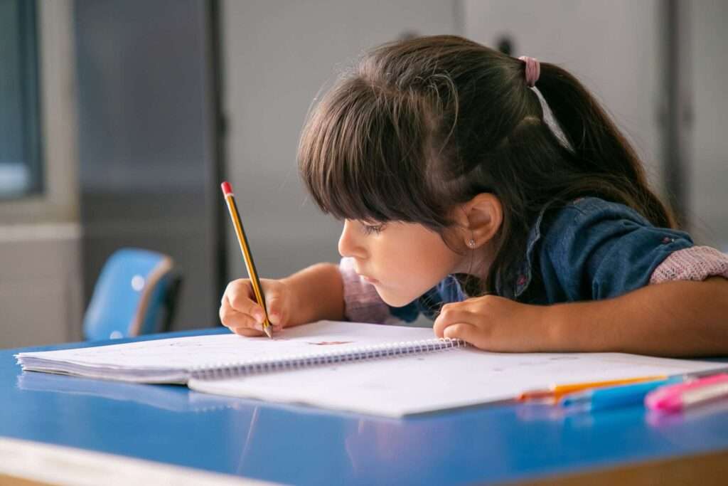 Школа майбутнього першокласника: українські діти зможуть відвідувати безплатні підготовчі заняття  Focused Haired Latin Girl Sitting School Desk Drawing Her Copybook UAinKrakow.pl